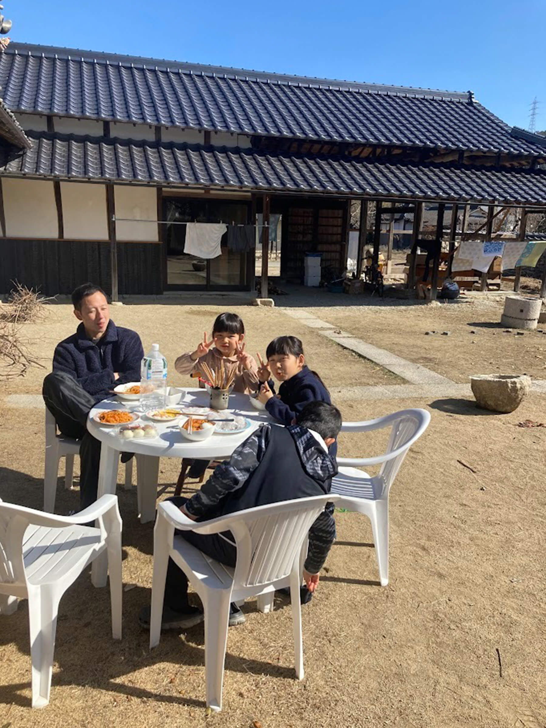 自宅の庭で子どもたちと食事をする梅村さん